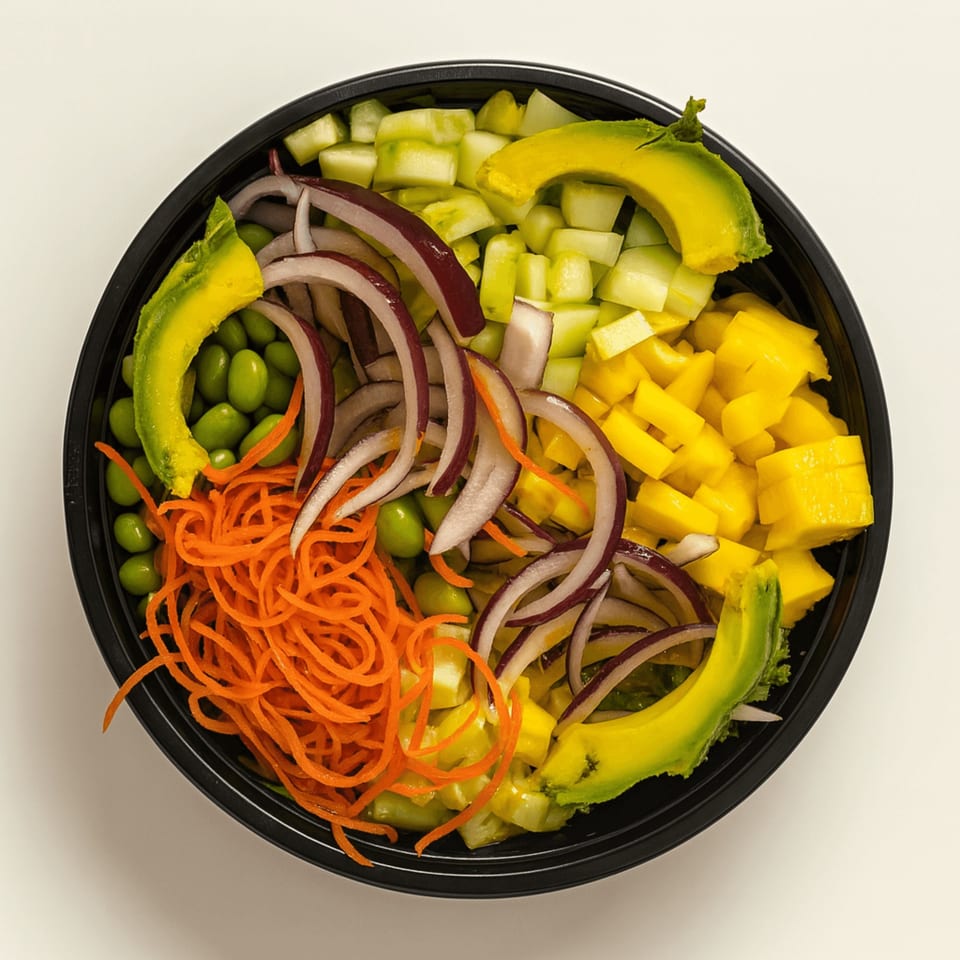 Overhead view of a colorful poke bowl with avocado, mango, cucumber, edamame, carrots, and red onion.